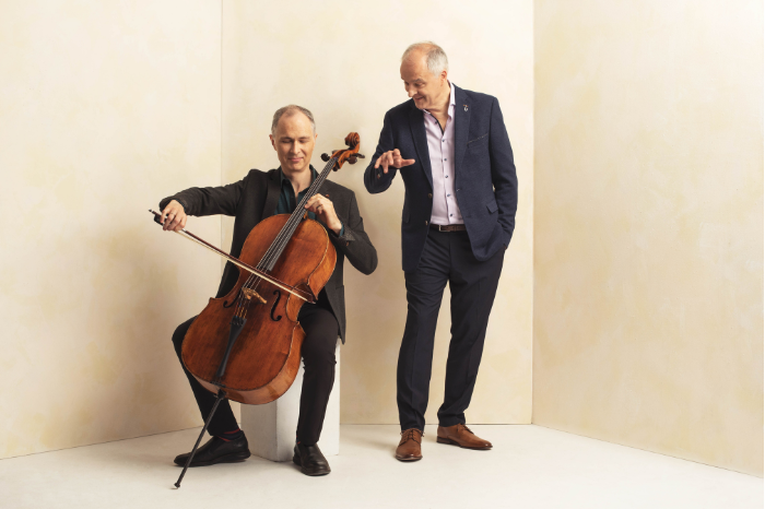 Dyachkov Saulnier Duo pose in a plain off-white room. One member plays cello.